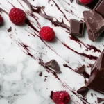 A delicious mix of chocolate pieces and fresh raspberries on a marble surface.