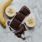 A top-down view of chocolate pieces and slices of banana arranged on a marble surface.