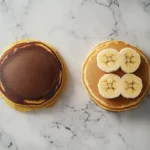 Top-down view of banana pancakes and regular pancakes side-by-side on a marble surface.